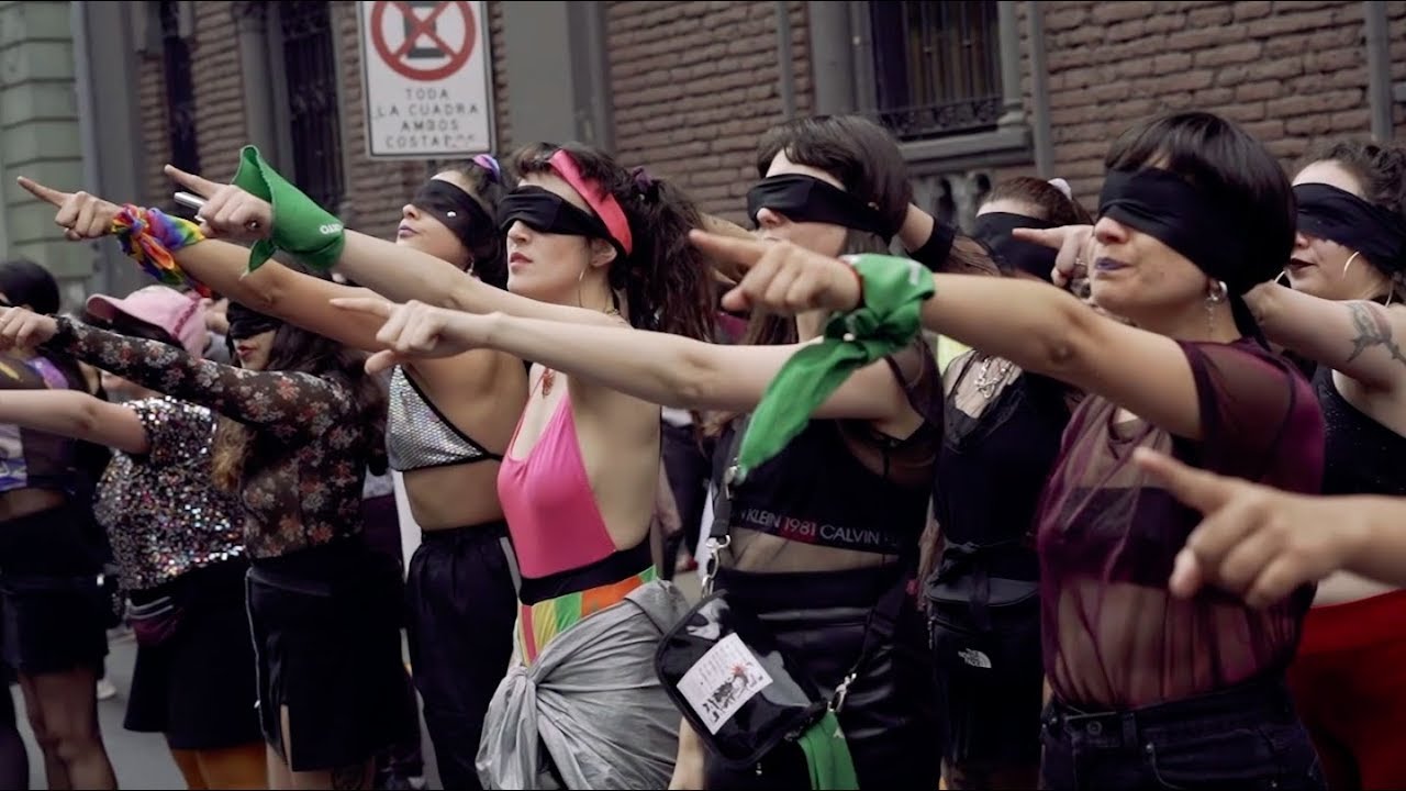Para cego ver: mulheres chilenas com os olhos vendados, apontando para frente. Elas usam um lenço verde em seus punhos, símbolo da luta pelo aborto gratuito e legal.